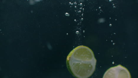 Lime-slices-fall-and-float-in-water-black-background-slow-motion.-Green-lime-slices-fall-and-float-in-water-black-background-slow-motion